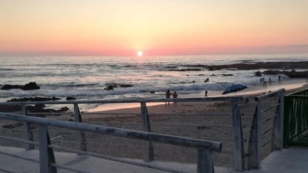 A beach with a sunset, people walking, and a concrete staircase leading down to the beach. - Pälm Hostal (Iquique)
