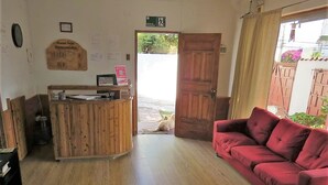 A reception area with a wooden desk, a red sofa, and a door leading outside. - Pälm Hostal (Iquique)