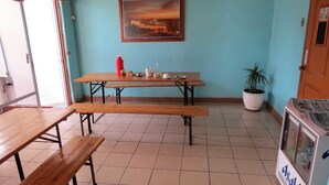 A room with wooden benches, a table with a red bottle, a potted plant, and a vending machine. - Pälm Hostal (Iquique)