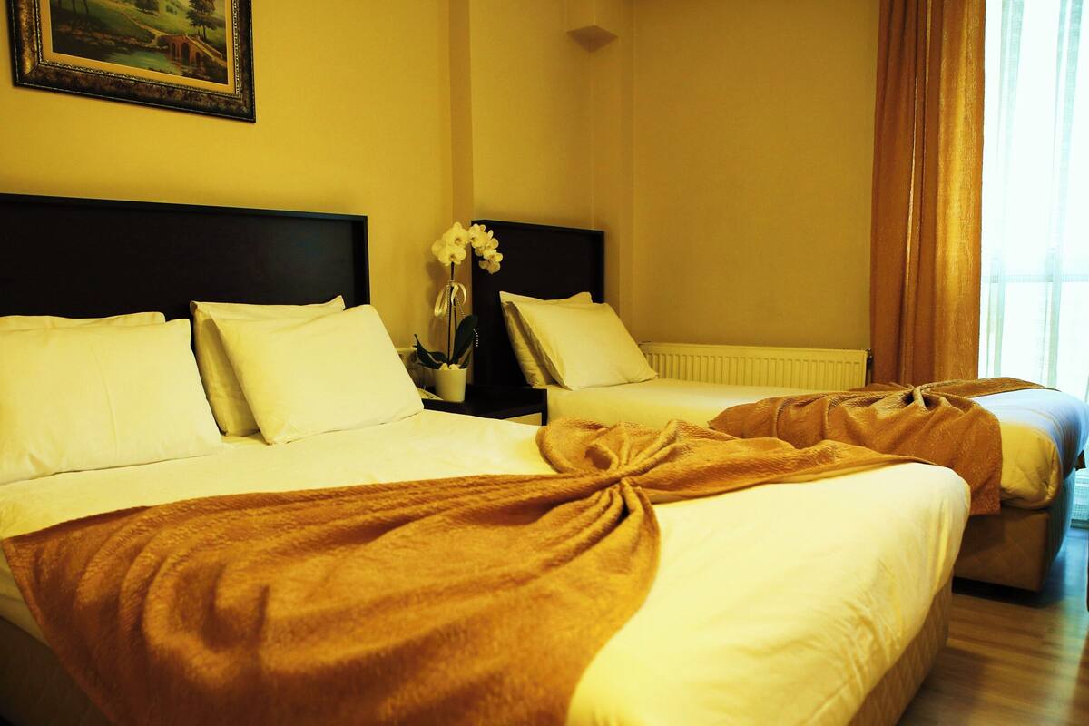 A hotel room with two beds, a nightstand, a framed picture on the wall, and a window with curtains.