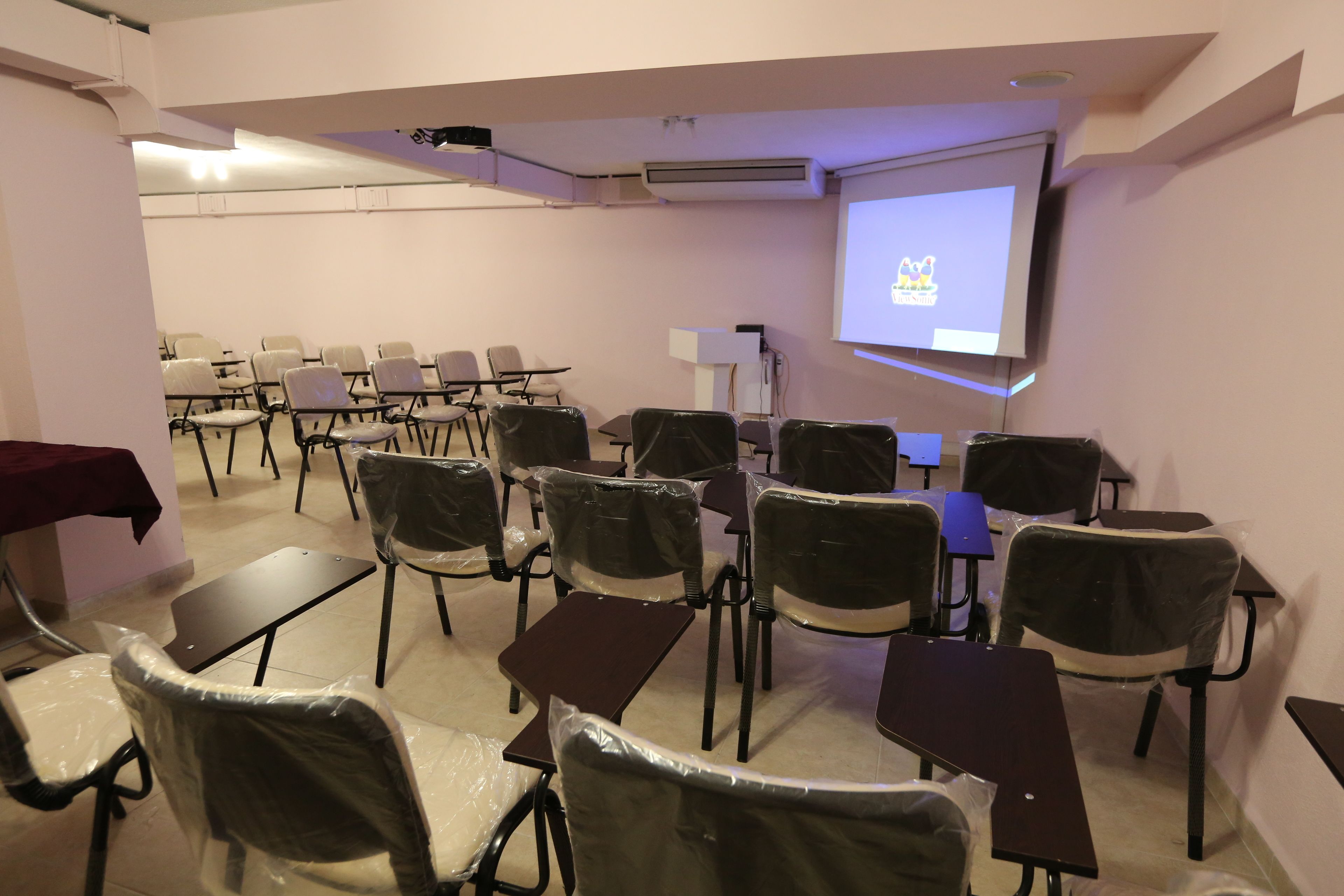 A conference room with rows of chairs, tables, and a projector screen displaying a logo.
