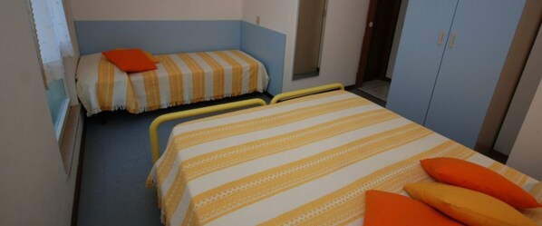 Una habitación con dos camas, una con una colcha a rayas y la otra con una lisa. Hay almohadas naranjas sobre las camas.