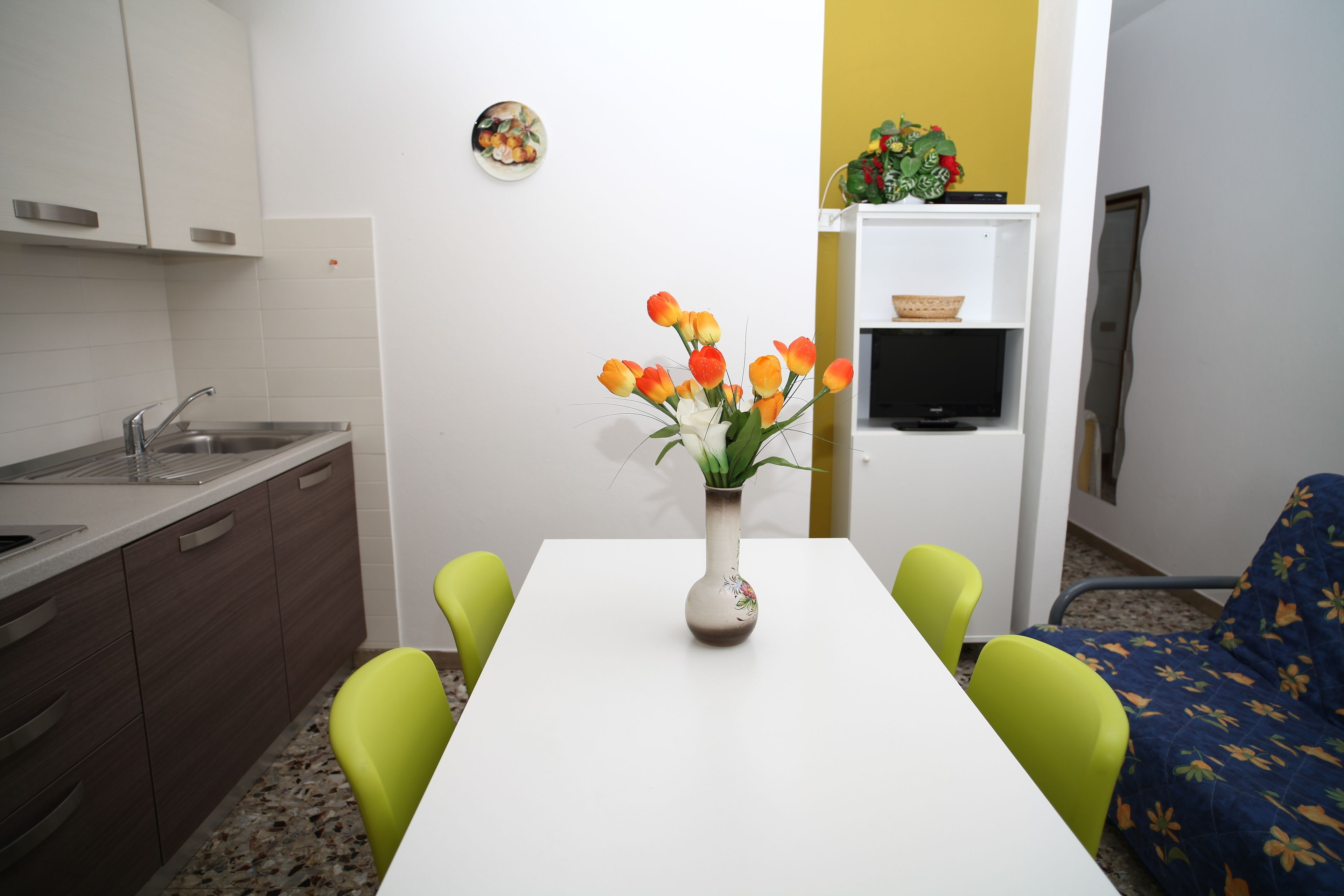 Een kleine keuken met een wit aanrecht, een spoelbak en een vaas met oranje bloemen op een tafel.