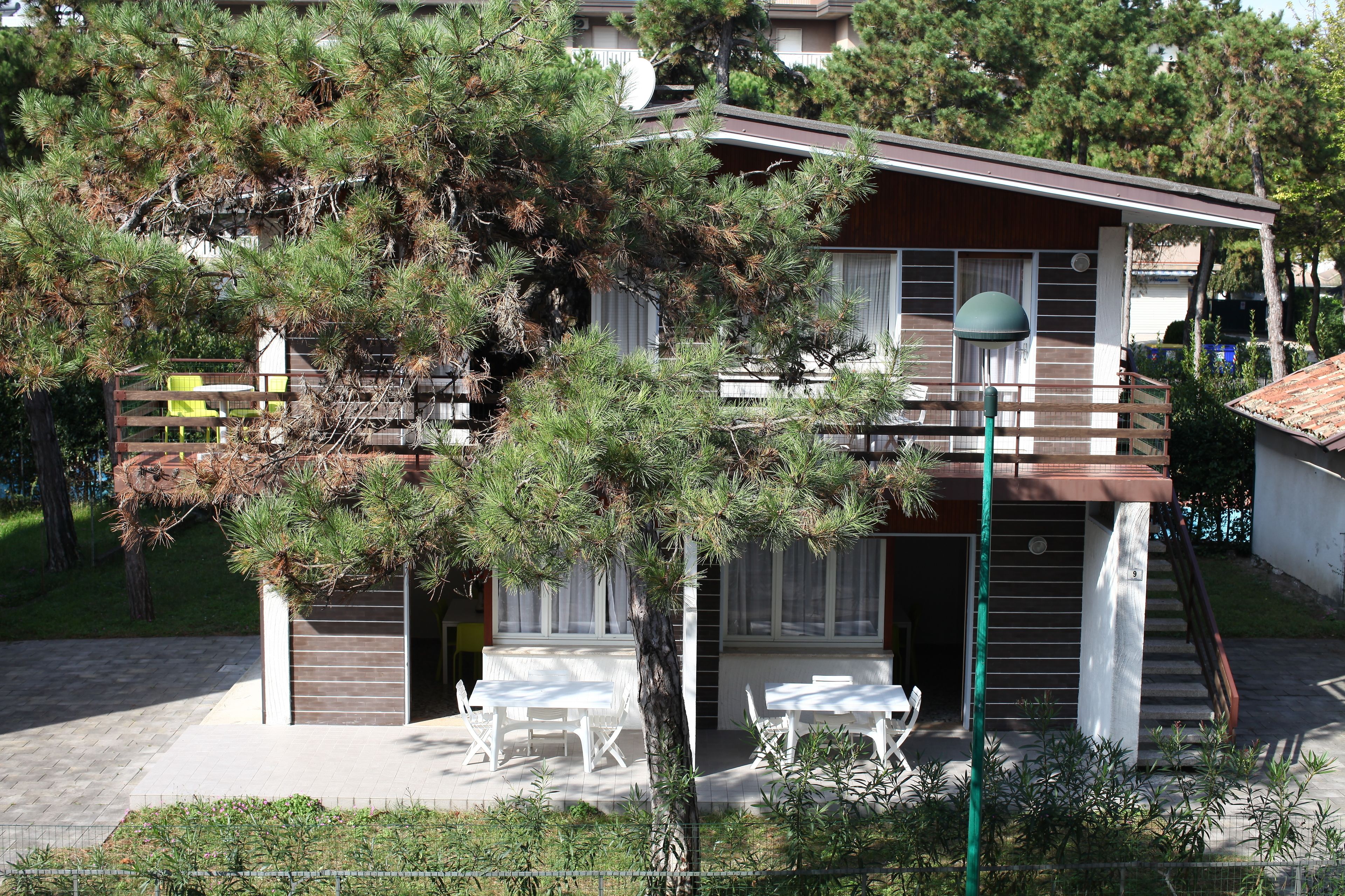 Ein zweigeschossiges Haus mit Balkon, überdachter Außenlounge und einer Treppe zum Obergeschoss.