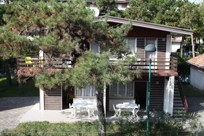 A two-story house with a balcony, a covered outdoor seating area, and a staircase leading to the upper floor. - Villa Morello (Lignano Sabbiadoro)