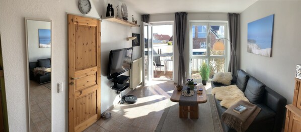 A living room with a wooden door, a black leather sofa, a coffee table, and a TV.