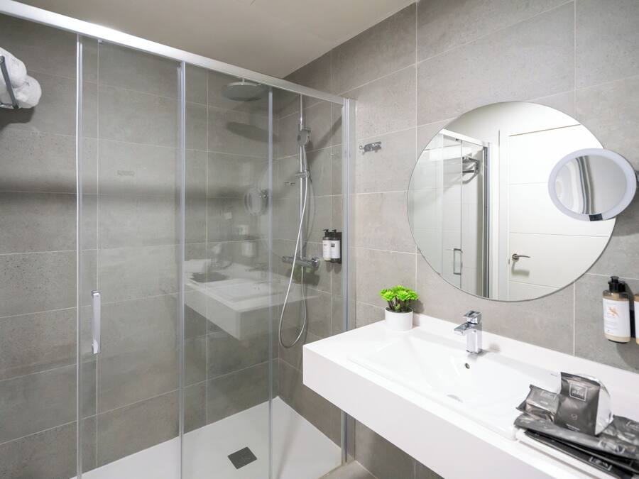 Un baño moderno con ducha envuelta en vidrio, un lavamanos blanco y un espejo redondo.