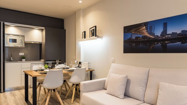 A modern kitchen with a microwave, stove, and dining area with a table and chairs. - Bilbao City Center by abba Suites (Bilbao)