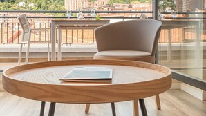 A modern room with a wooden round table and two chairs, a large window with a view of a cityscape and greenery. - Bilbao City Center by abba Suites (Bilbao)