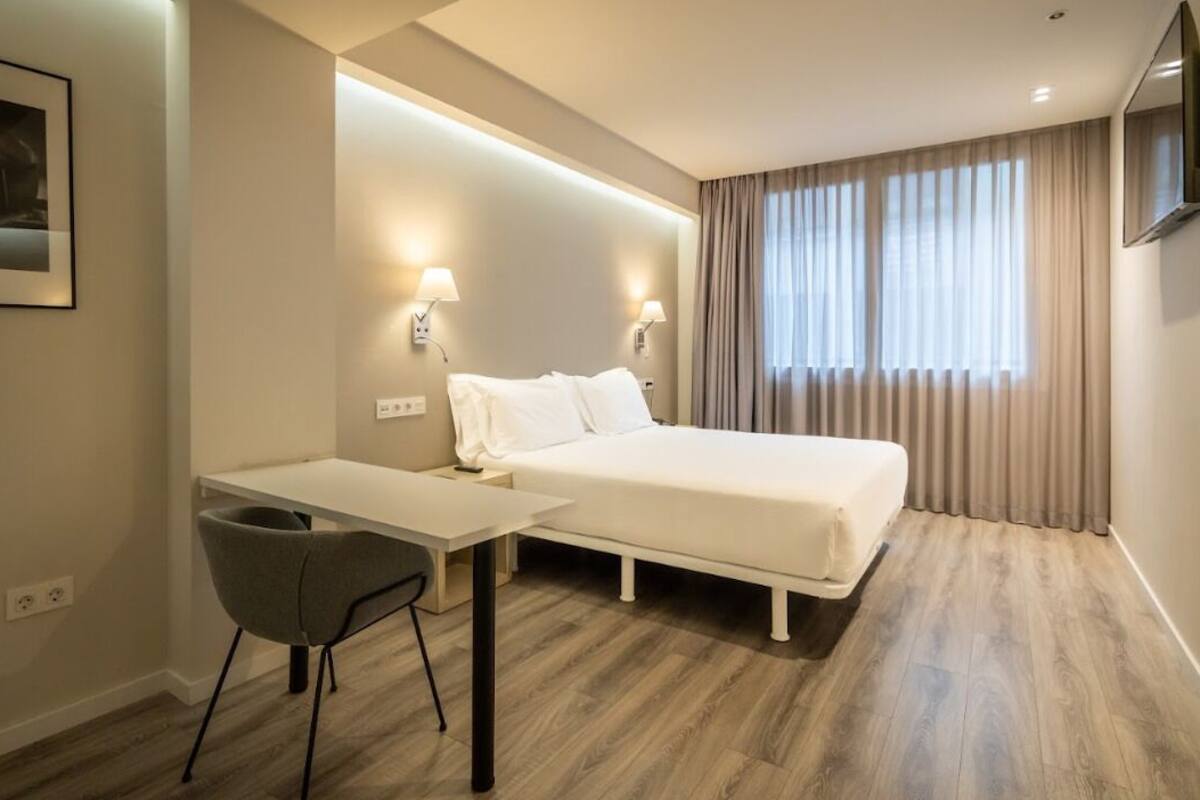 Habitación de hotel con una cama, un escritorio, una silla y un televisor montado en la pared.