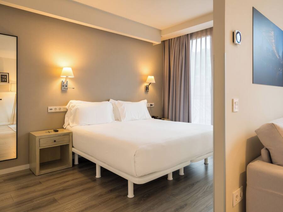 Una habitación de hotel con una cama grande, mesitas de noche, un escritorio, una silla y un espejo amplio.