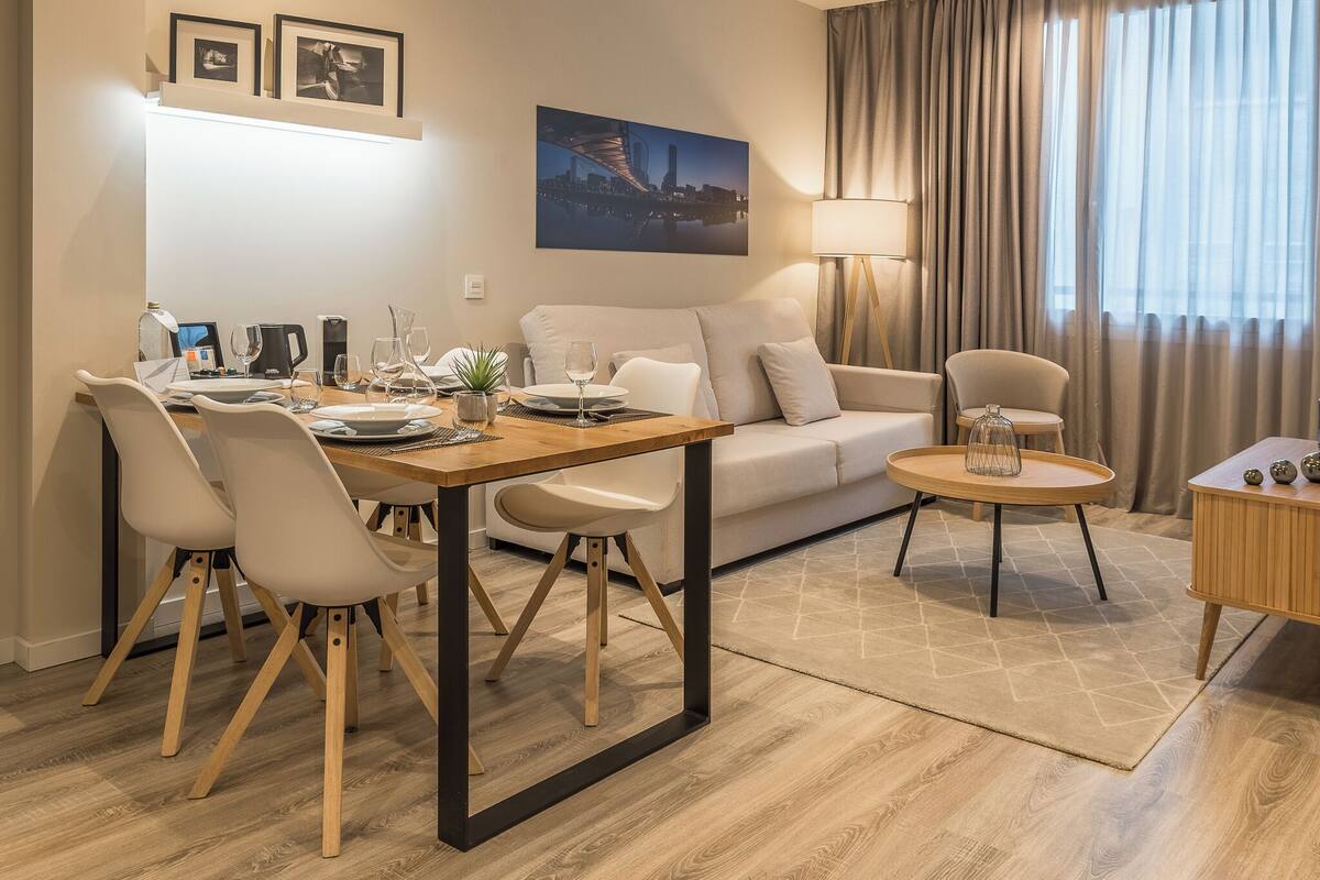 Una sala de estar moderna con comedor, que incluye un sofá, sillas, una mesa de centro y una lámpara.