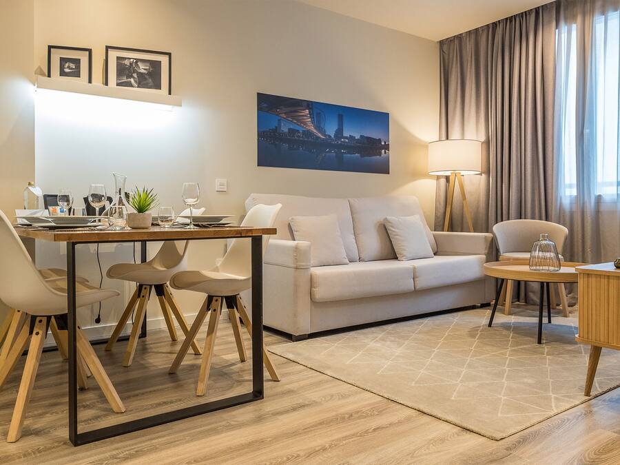 A modern living room with a dining area, a sofa, a lamp, and a painting on the wall.