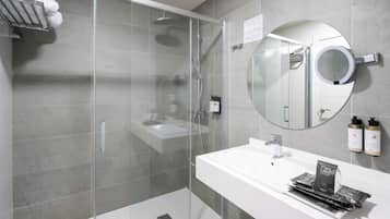 Un baño moderno con ducha de vidrio, un lavabo blanco y un espejo redondo.
