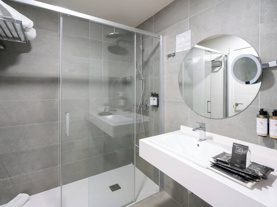 Un baño moderno con ducha de vidrio, un lavabo blanco y un espejo redondo.