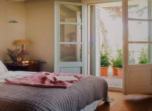 Un dormitorio con cama, mesita de noche, lámpara y vistas al exterior a través de una puerta.