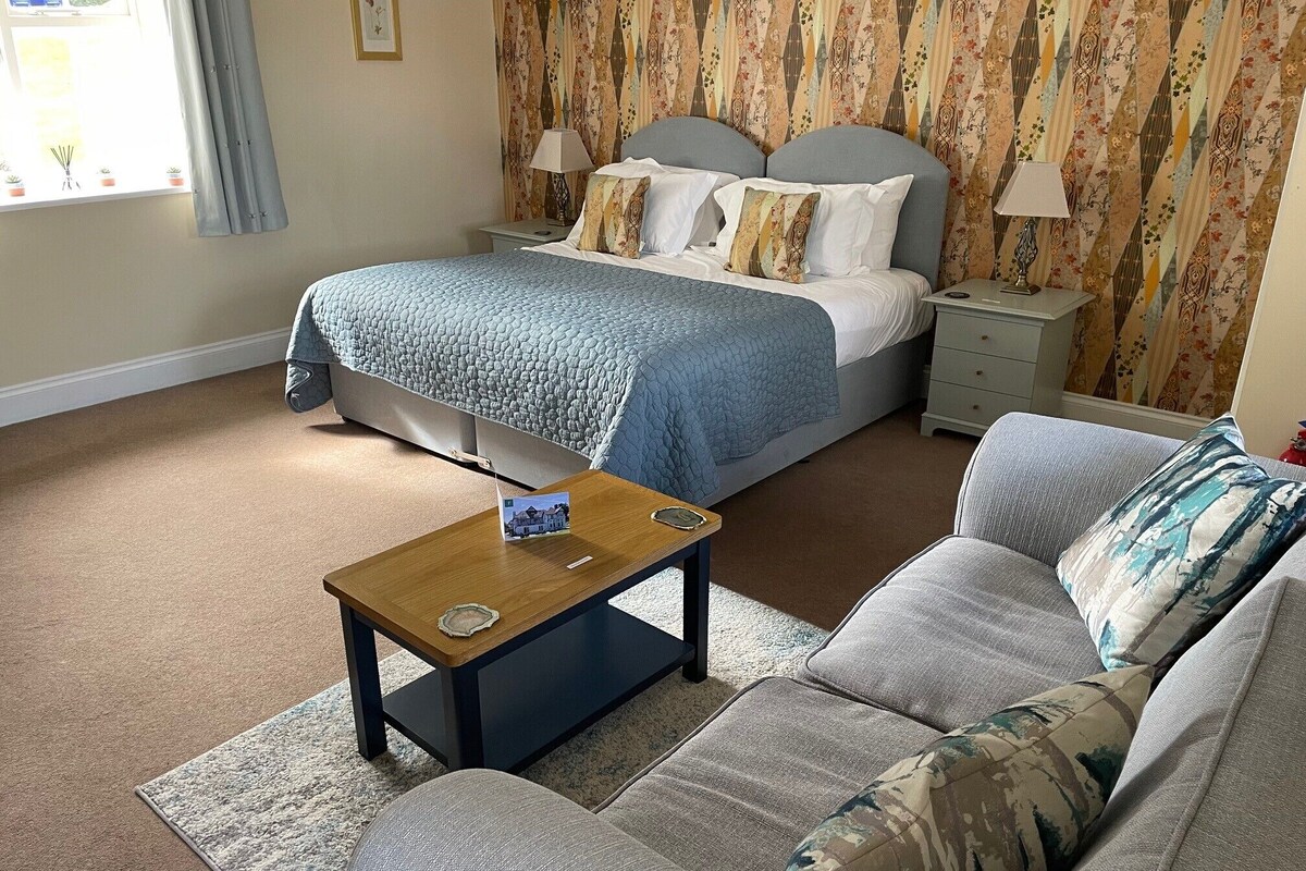 A bedroom with a bed, a nightstand, a sofa, and a small table with a lamp.