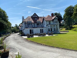 A large, two-story house with a prominent balcony, a driveway leading to the entrance, and a well-maintained lawn. - The Penrallt Hotel (Cardigan)