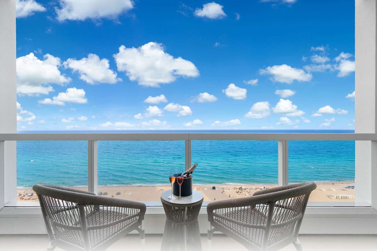 Een balkon met rieten stoelen en een tafel, met uitzicht op een strand en de oceaan.
