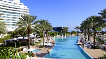 A large swimming pool surrounded by palm trees and lounge chairs, with a modern building in the background.