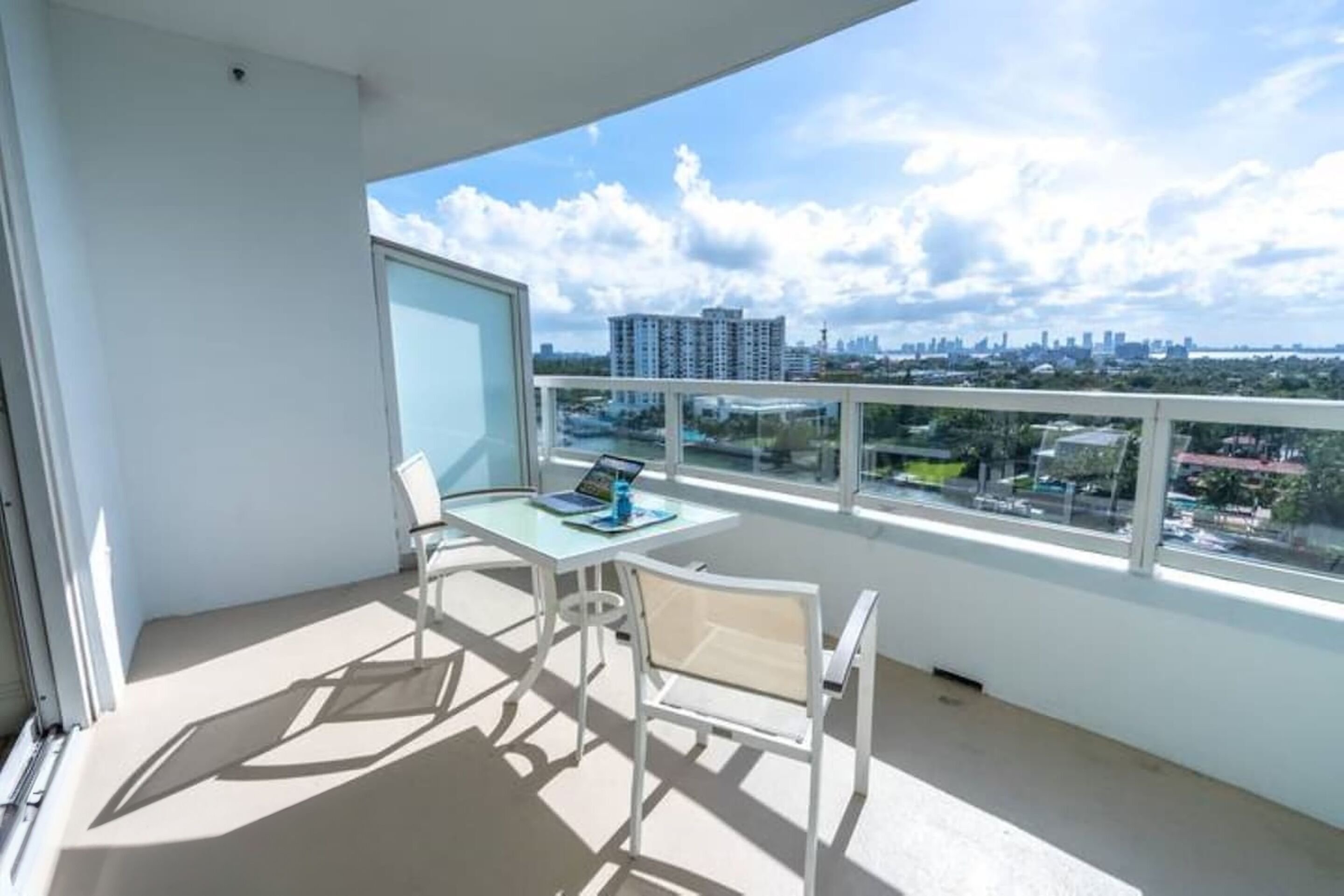 A balcony with a table and chairs, a laptop, and a view of a cityscape.