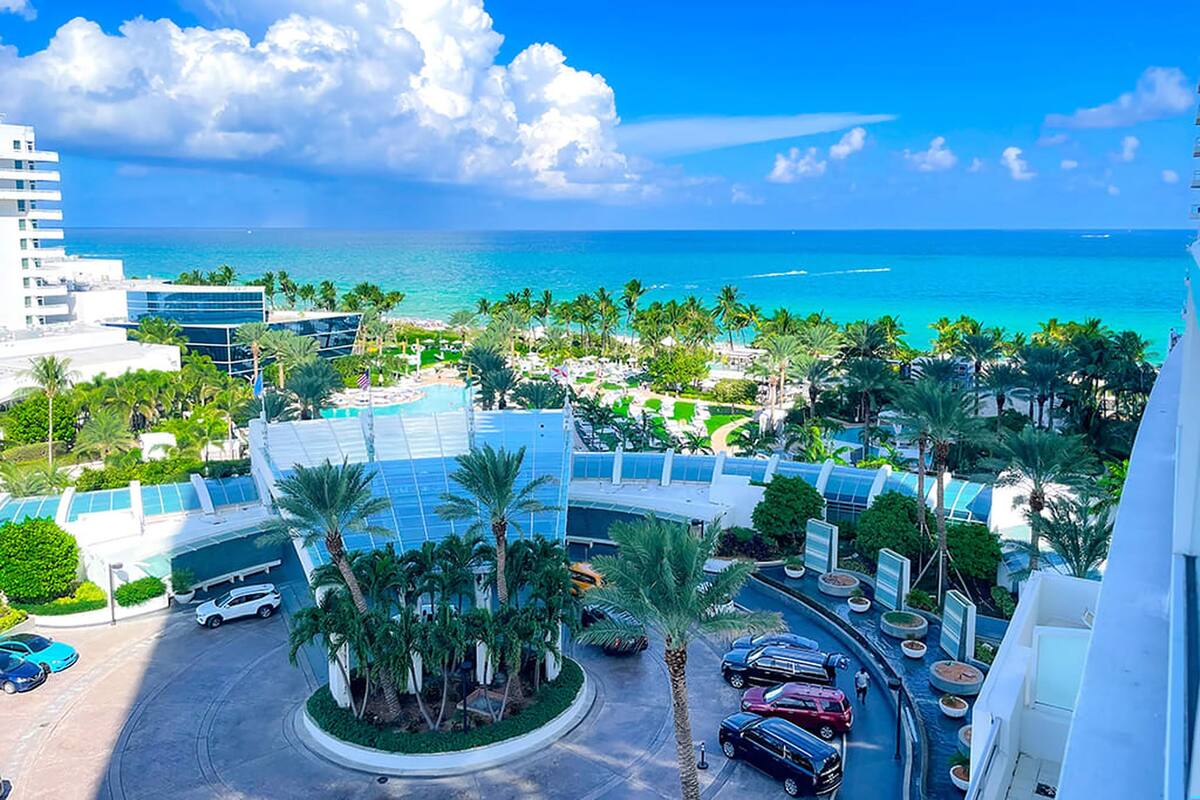 Een resort met een zwembad, palmbomen en uitzicht op zee.