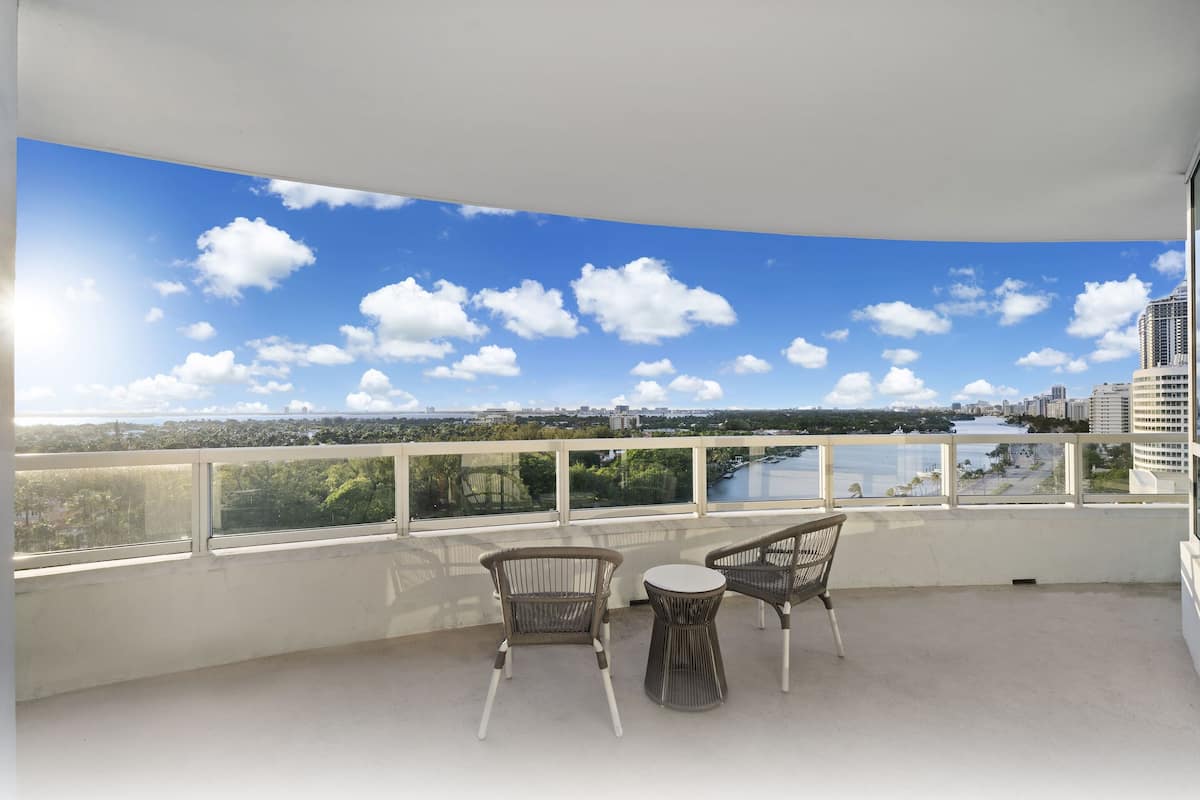 Een balkon met twee rieten stoelen en een kleine tafel, met uitzicht op een stadsgezicht met een rivier en gebouwen.