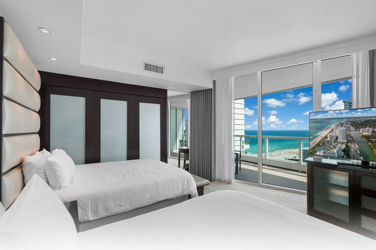 Een moderne hotelkamer met een groot bed, een televisie en een balkon met uitzicht op het strand en de oceaan.
