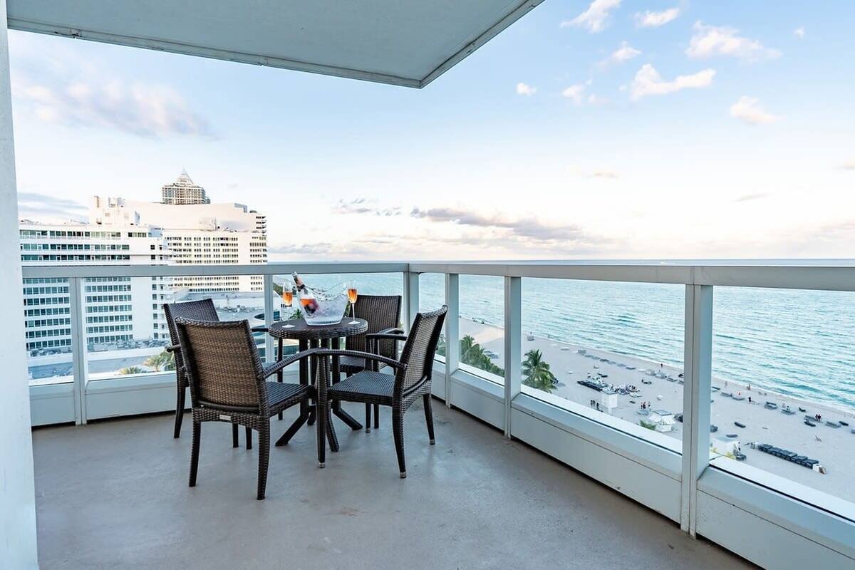 Een balkon met rieten stoelen en een tafel, met uitzicht op een strand en stadsbeeld.