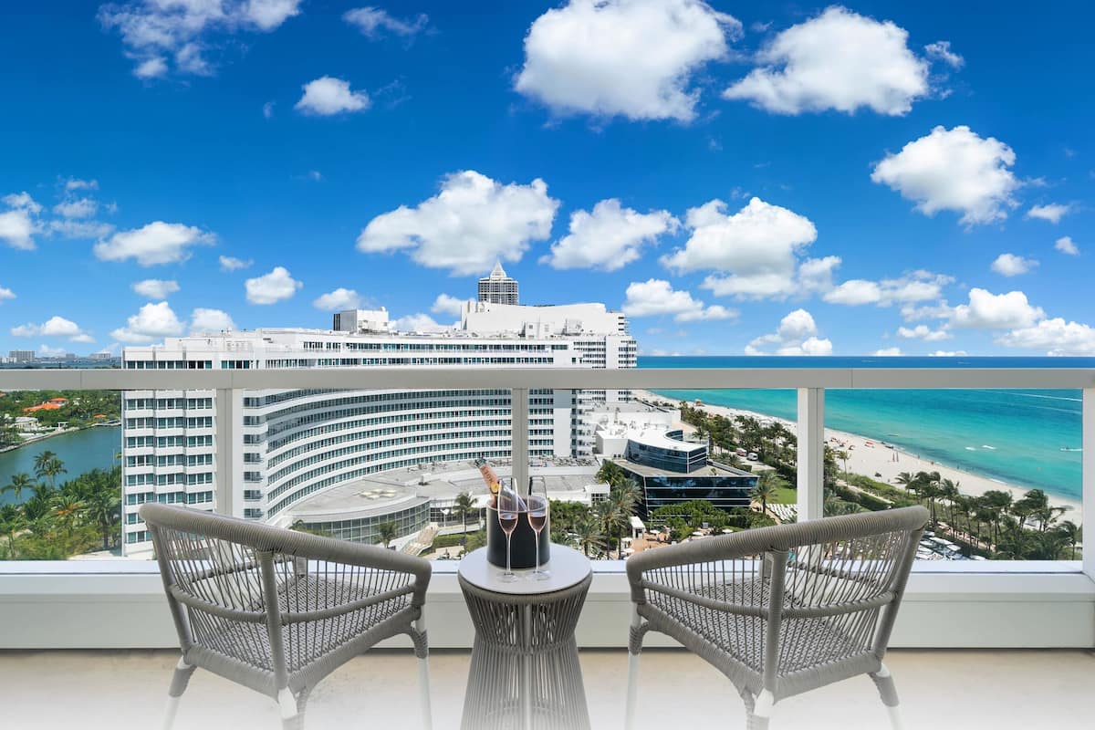 Een balkon met rieten stoelen en een tafel, met uitzicht op een strand en een modern hotelgebouw.