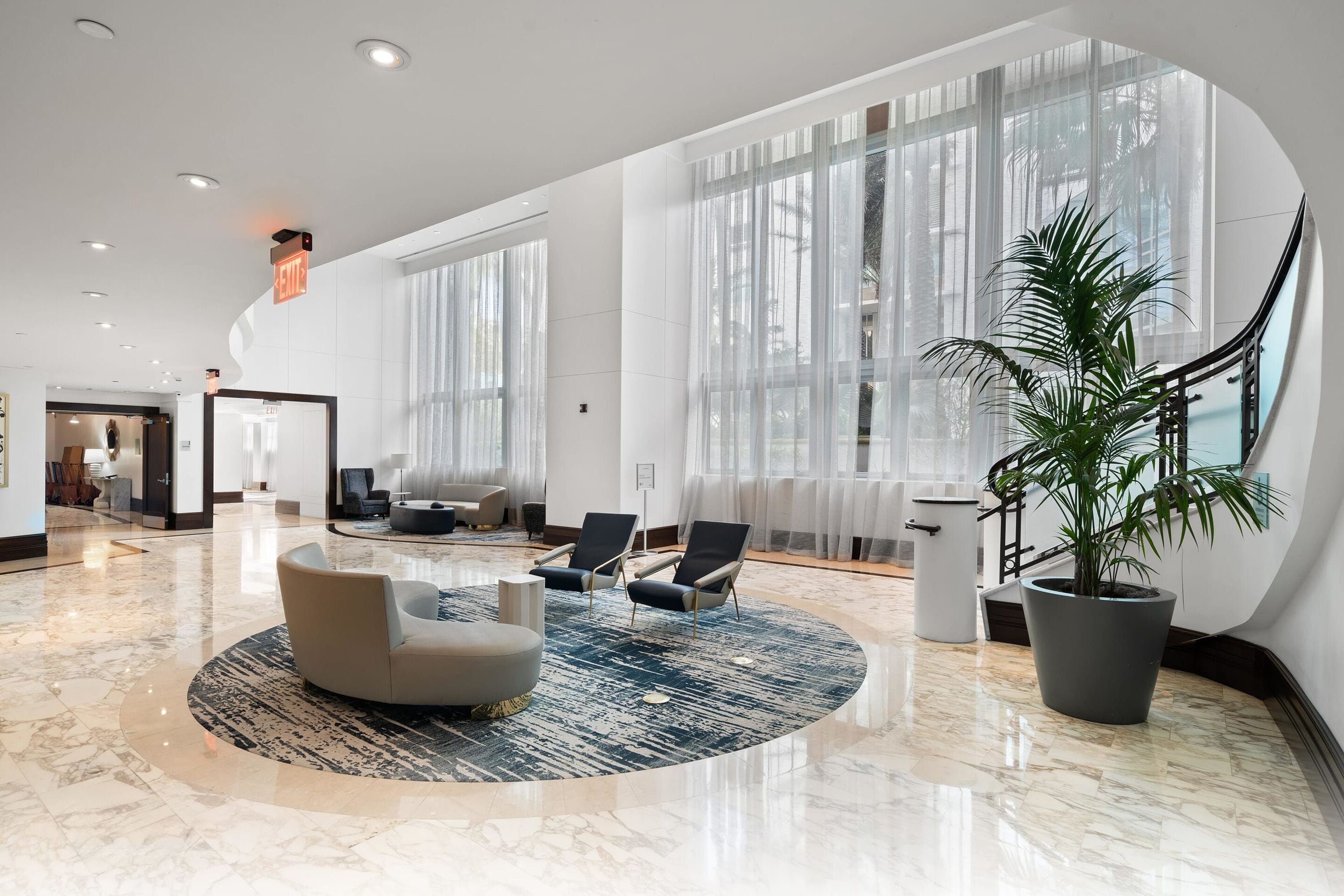 A spacious lobby with a marble floor, a round seating area, and large windows with sheer curtains.
