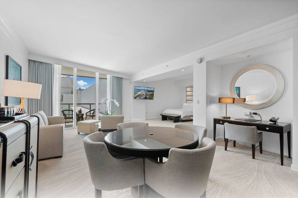 Een moderne hotelkamer met een ronde eettafel, een bank, een bureau en een grote spiegel.