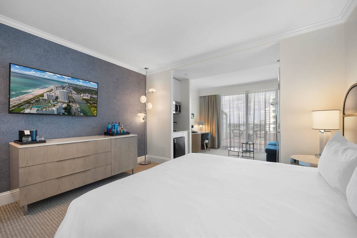 Hotelkamer met een groot bed, een tv aan de muur, een bureau met stoel, en een balkon met uitzicht op de stad.