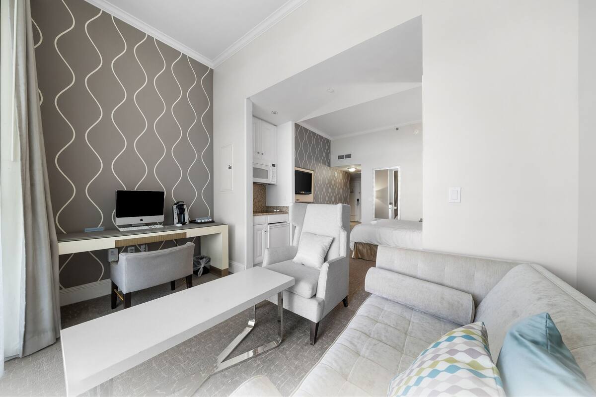 Een moderne woonkamer met een bank, een bureau met een computer en een stoel. Achtergrond is een keuken.