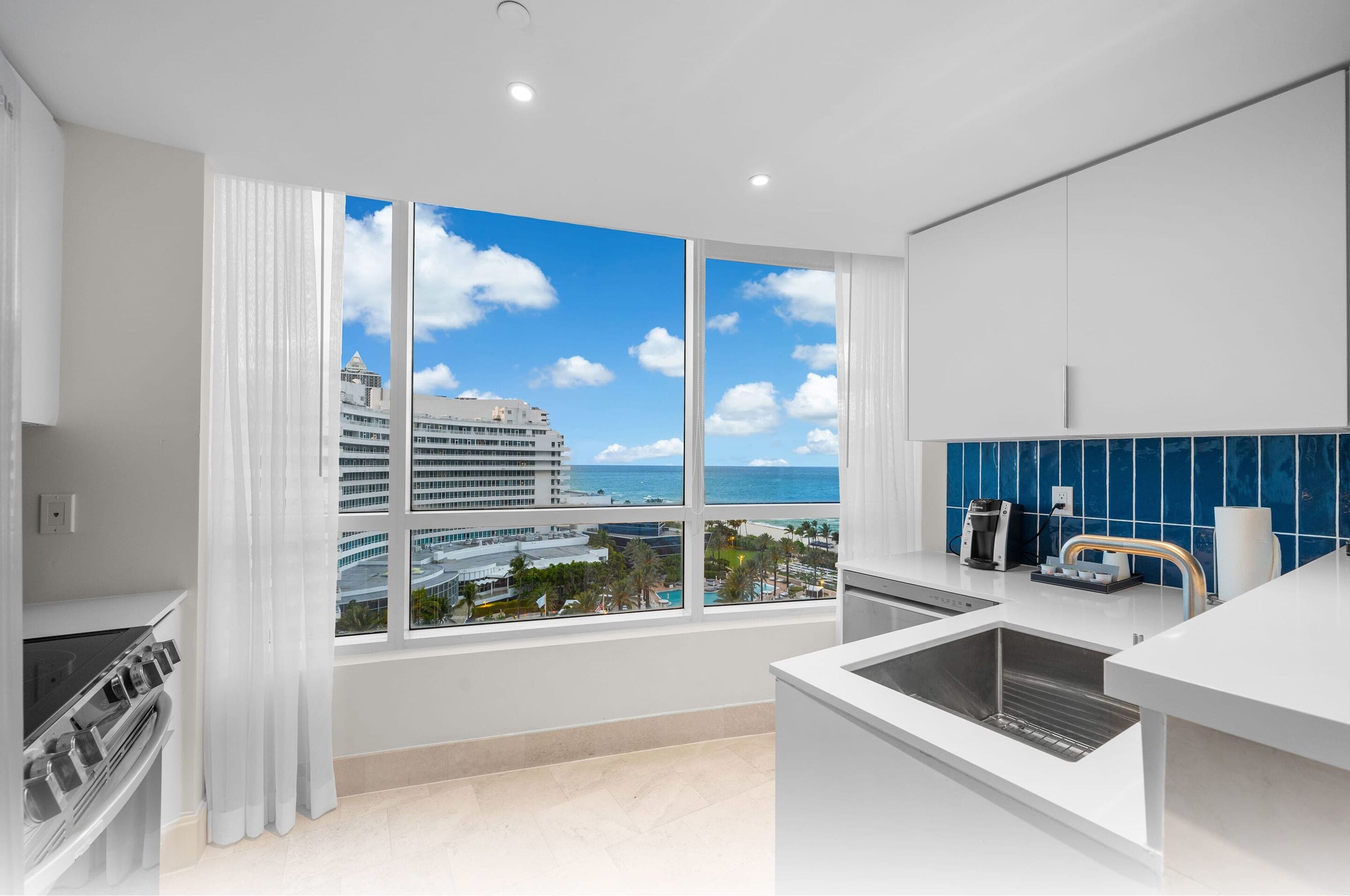 A modern kitchen with a large window offering a view of a cruise ship and a beach.