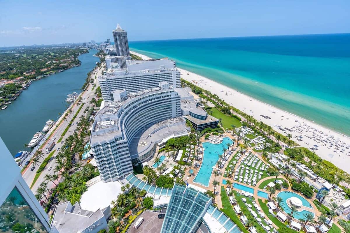 Een hoog hotel met zwembad, een strand en een jachthaven.