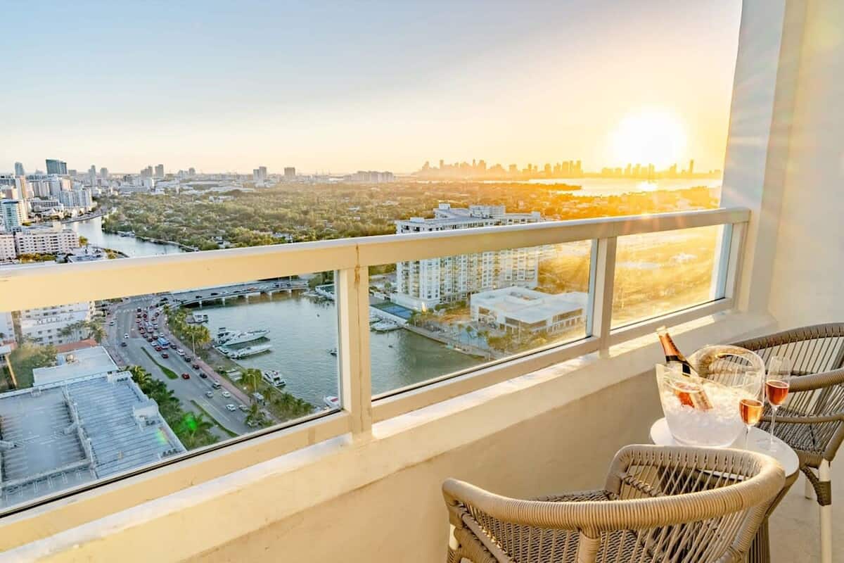Een balkon met rieten stoelen, een tafel met champagnefles en uitzicht op een stadslandschap en rivier.