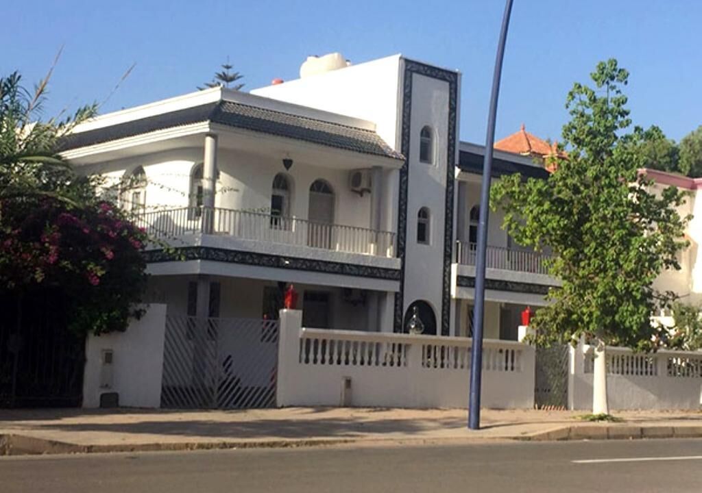 Un immeuble de deux étages doté d’un balcon, d’une entrée sécurisée par un portail et surplombant un ciel dégagé.