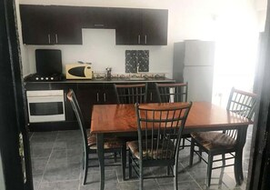 A compact kitchen with dark cabinets, a stove, and a dining table with chairs.