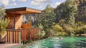 Un área de piscina moderna con terraza de madera y una estructura de vidrio.