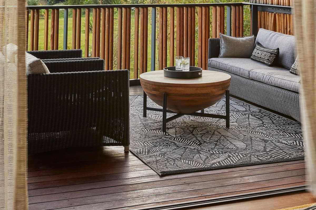A balcony with wicker furniture, a round wooden table, and a view of a forested hill.