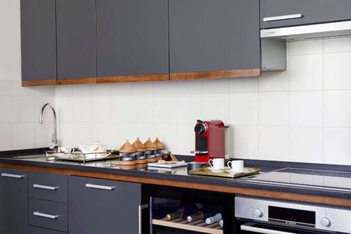 A modern kitchen with dark cabinets, a stainless steel sink, a coffee machine, and wine bottles stored under the counter.