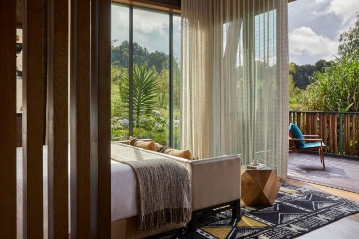 A bedroom with a bed, a view of greenery outside, and a balcony with a chair.