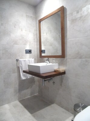 Ett modernt badrum med ett rektangulärt handfat, en spegel med träram och en liten hylla med en korg.