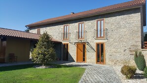 A stone building with a tiled roof, a wooden door, and a small tree in the front yard.