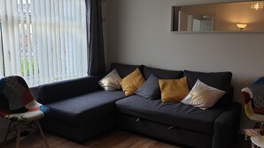 Een moderne woonkamer met een donkergrijze modulaire bank, gestreepte kussens, een bijzettafeltje met een dienblad vol ontbijtartikelen en een raam met dunne gordijnen.