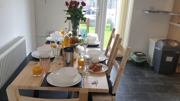 Een ontbijttafel gedekt met borden, glazen, een vaas met bloemen en een schaal fruit.