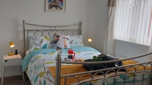 Een netjes opgemaakt bed met een bedsprei met dessin, een nachtkastje met een lamp, en een afbeelding van de Eiffeltoren aan de muur.