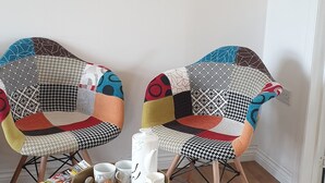 Twee stoelen met kleurrijke, lappendeken bekleding, een klein rond tafeltje met een schaal eten en drinken, en een tijdschrift op de vloer.