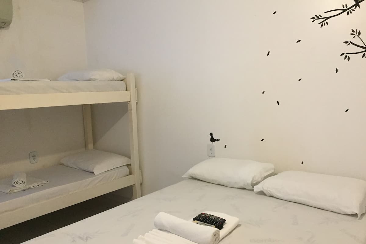 Quarto com beliches, roupa de cama branca e controle remoto no beliche inferior.